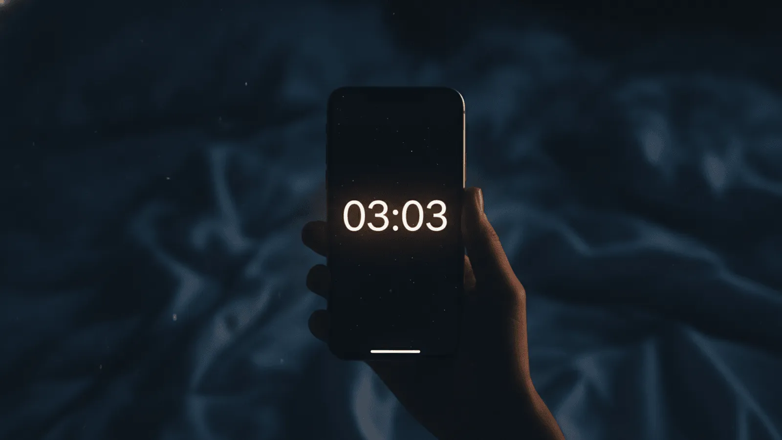 Relógio digital de cabeceira marcando 03:03 em números vermelhos, num quarto escuro com a luz da rua entrando pela fresta da cortina